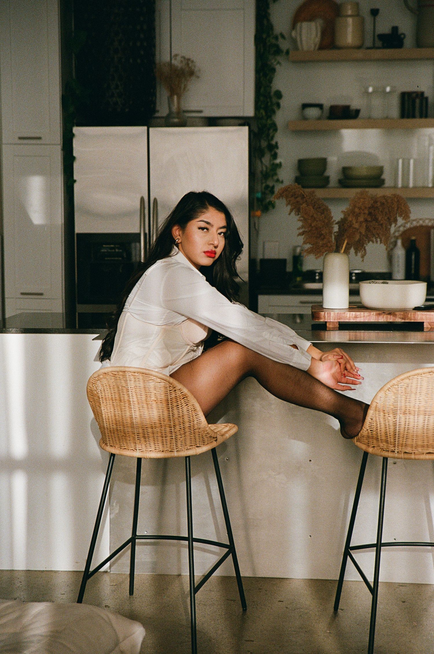Woman on a bar stool kicking her feet up and looking at the camera.