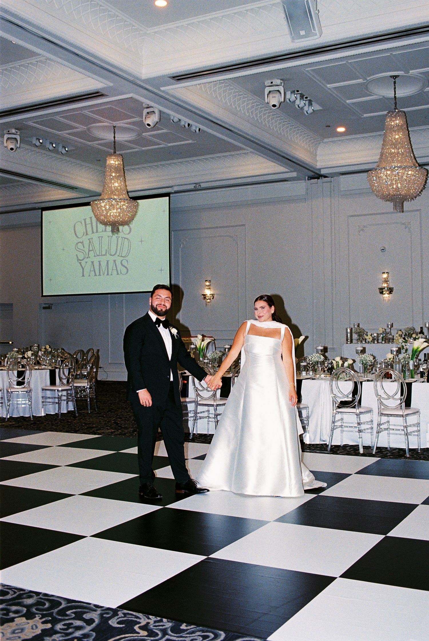 Bride and groom pose together holding hands on the dance floor surrounded by black and white tiles.