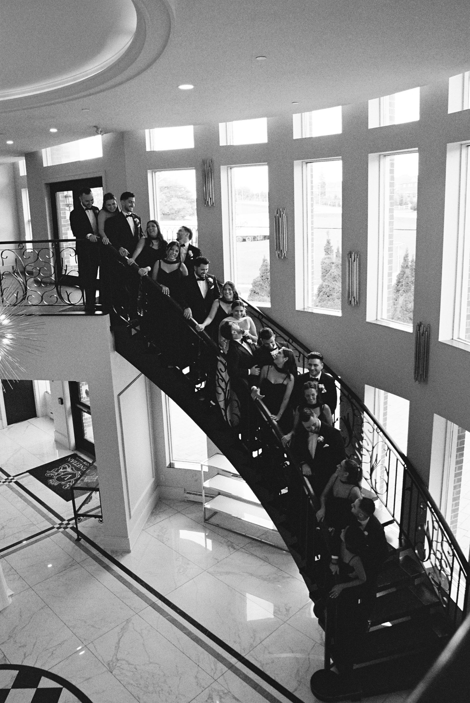 Bride, groom, bridal party, and groomsmen stand together on a grand staircase at the Royal Venetian Mansion in Vaughan, Ontario.