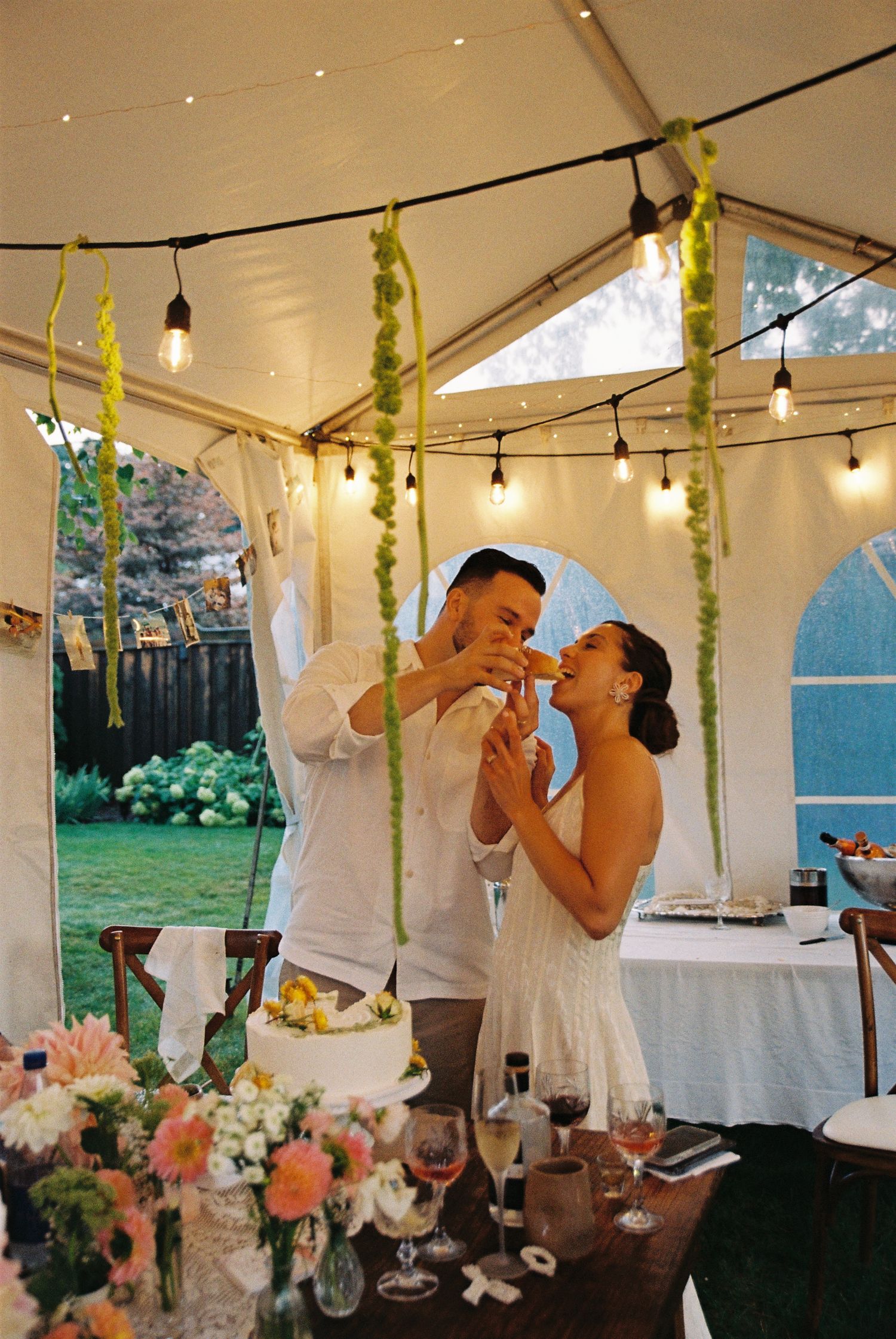 Bride and groom cut the first slice of cake and feed it to each other in their backyard wedding reception.