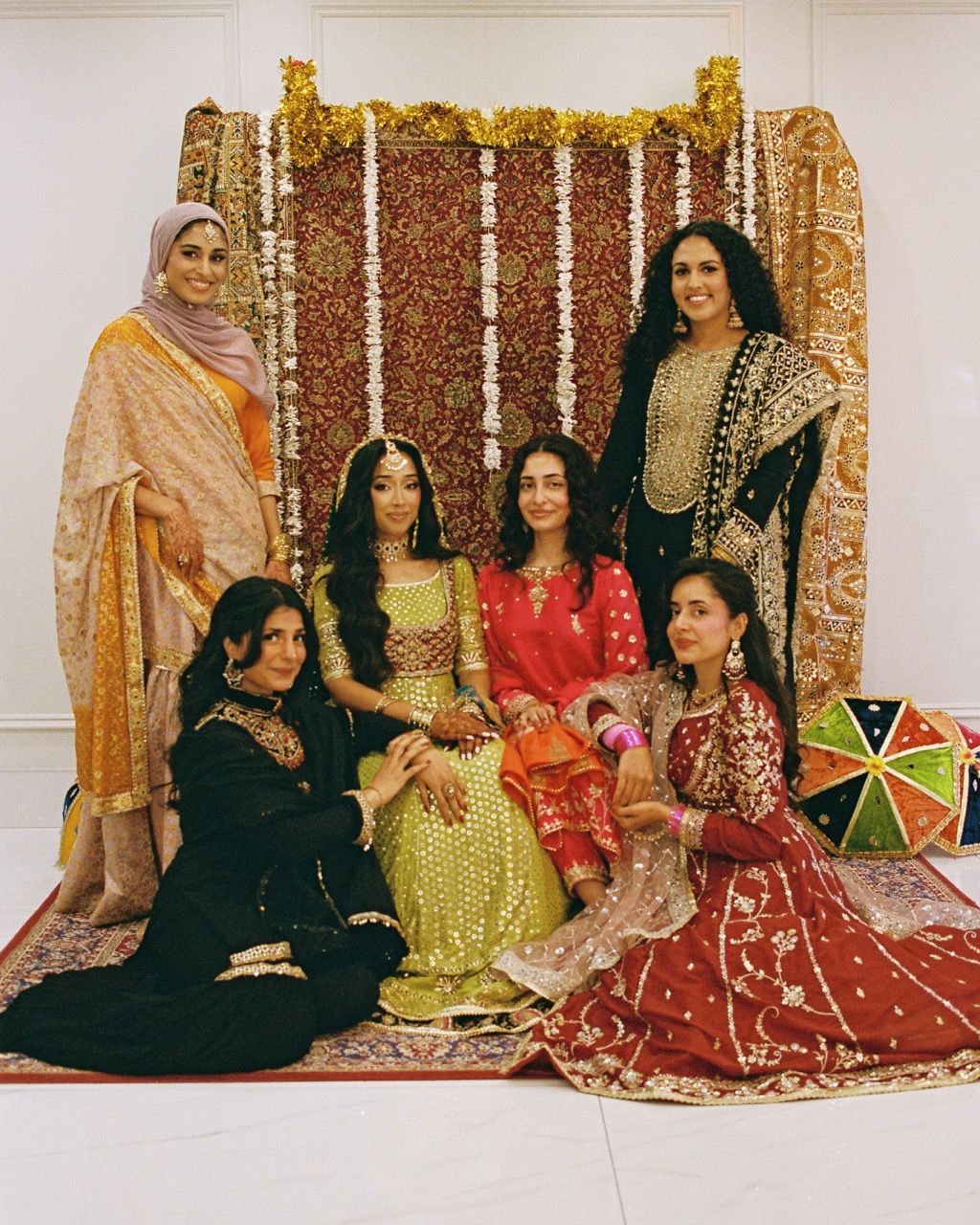 Bride and bridesmaids posed together in front of a red persian rug back drop.