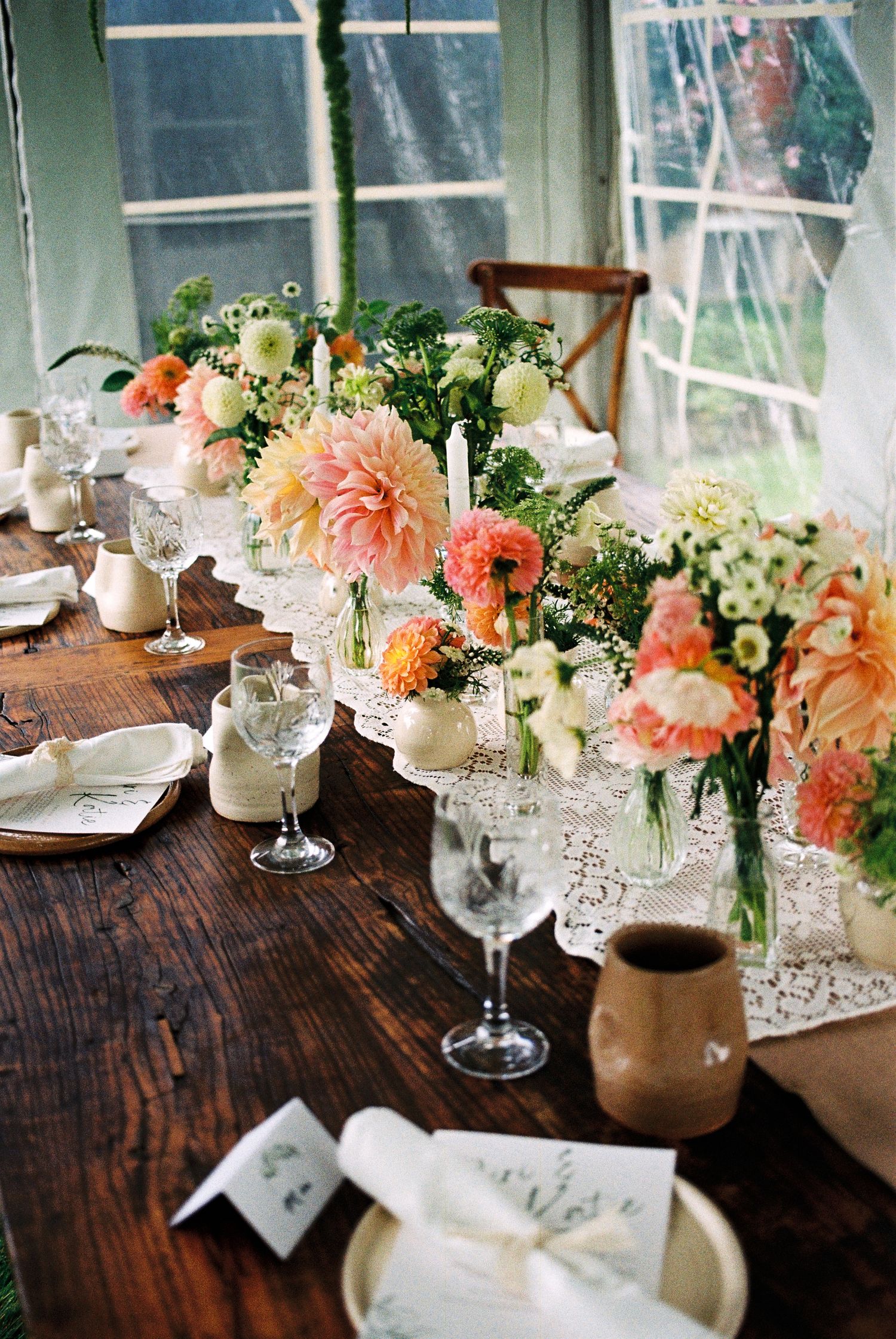 Elopement reception table covered in clay plates, mugs, wine glasses, lace fabric, and florals.