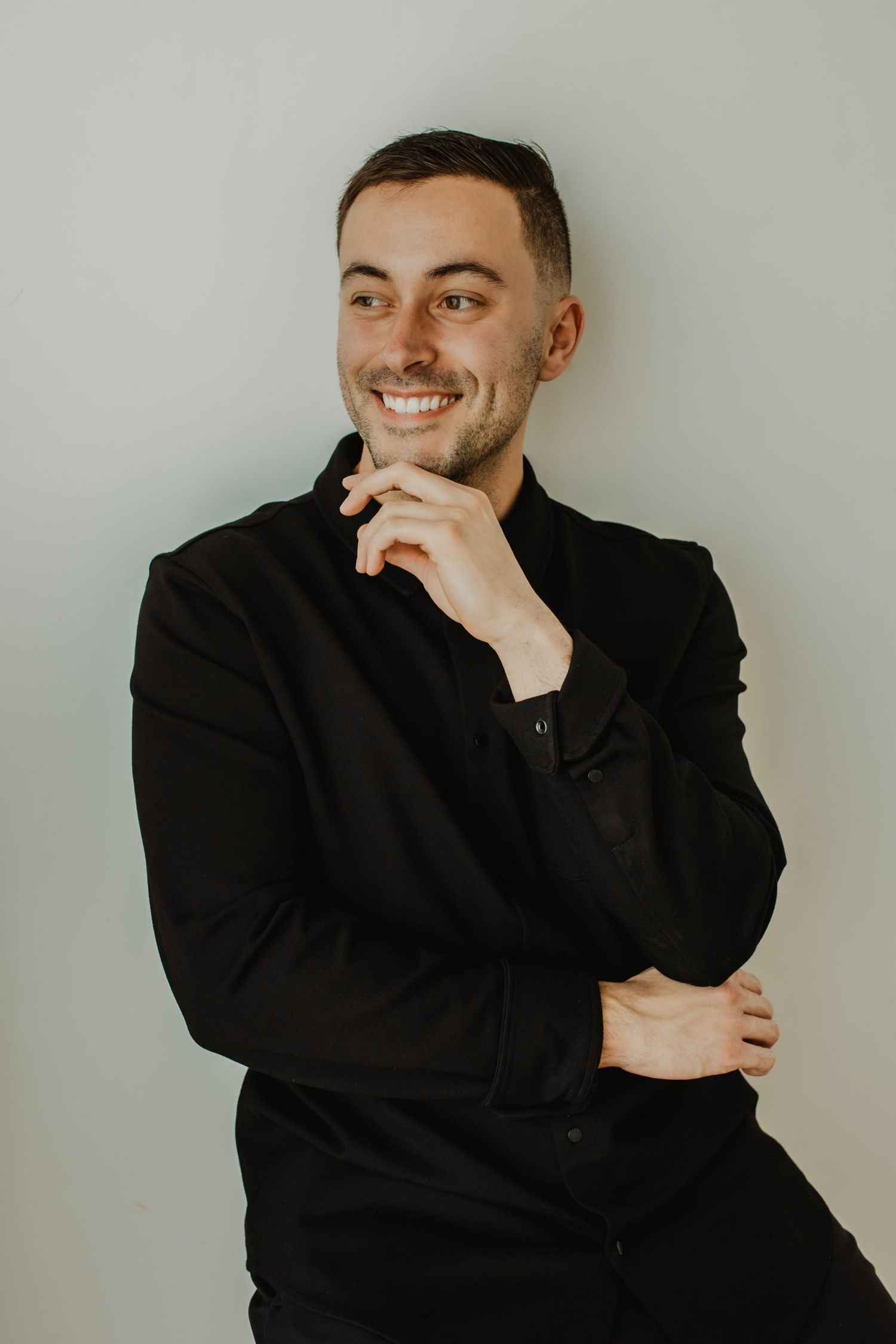 Person in black attire poses against neutral gray background with expressive gestures.