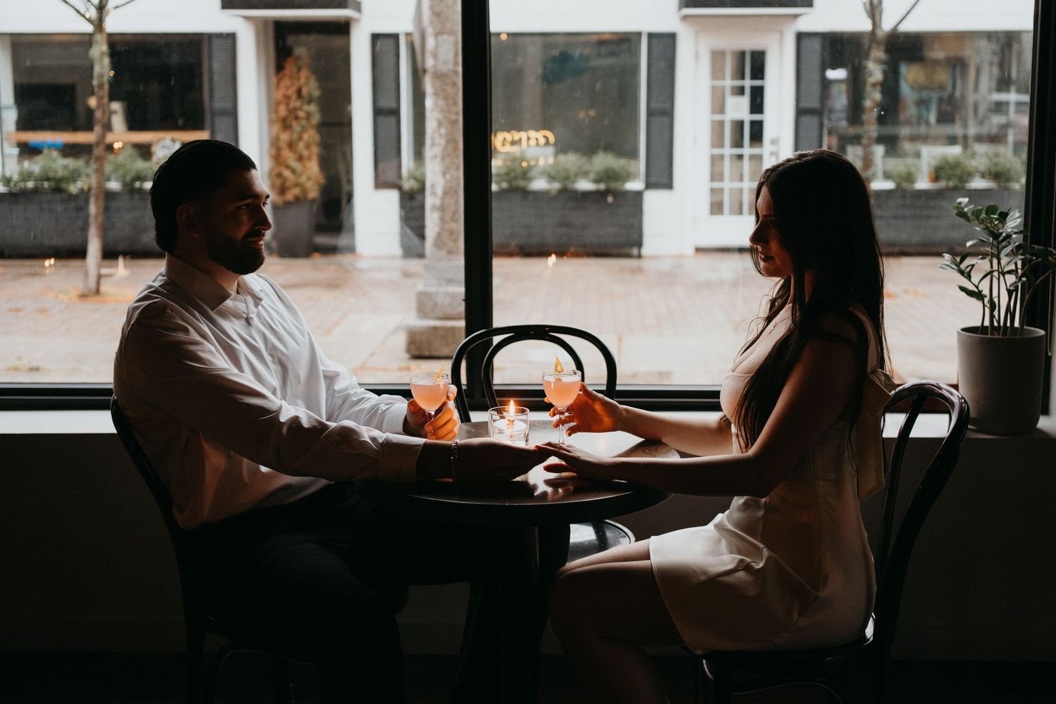 Silhouettes of people dining by window in moody restaurant setting.