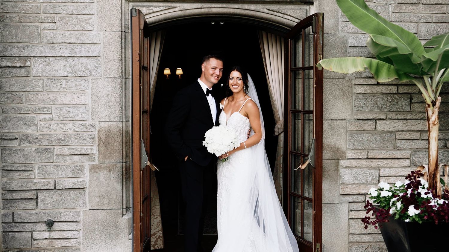 Wedding couple poses in front of a stone church entrance with elegant architecture.
