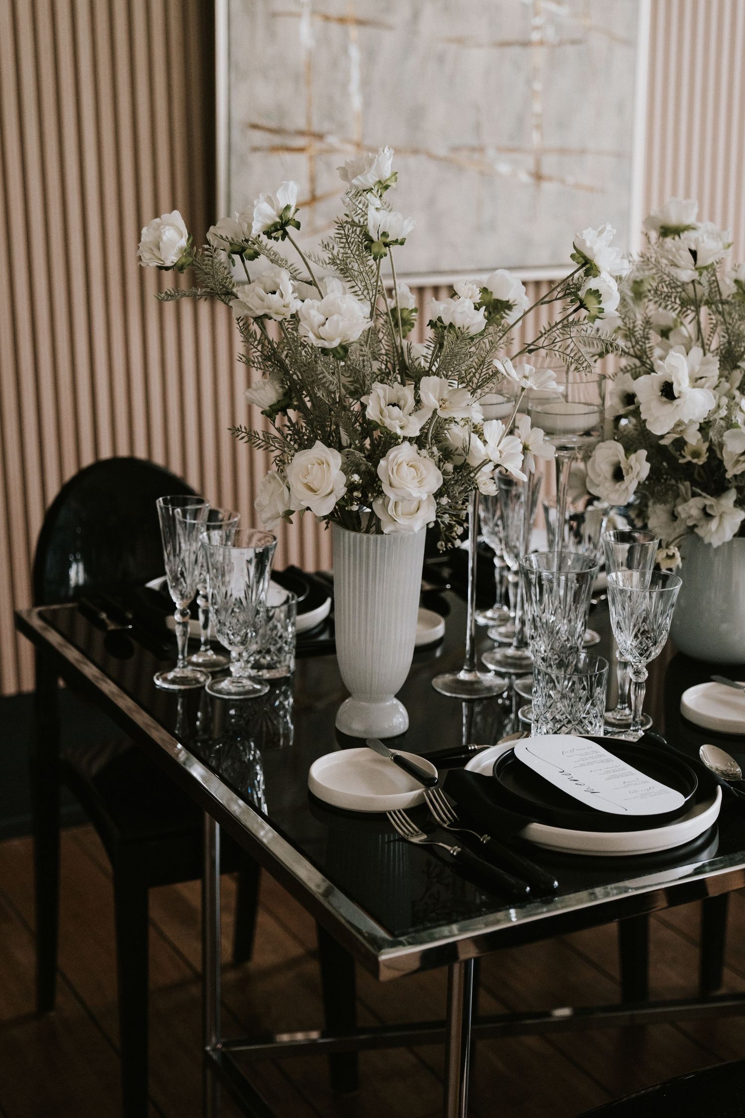 Elegant wedding table setting with white floral centerpieces, crystal glassware, and black charger plates on dark tables.