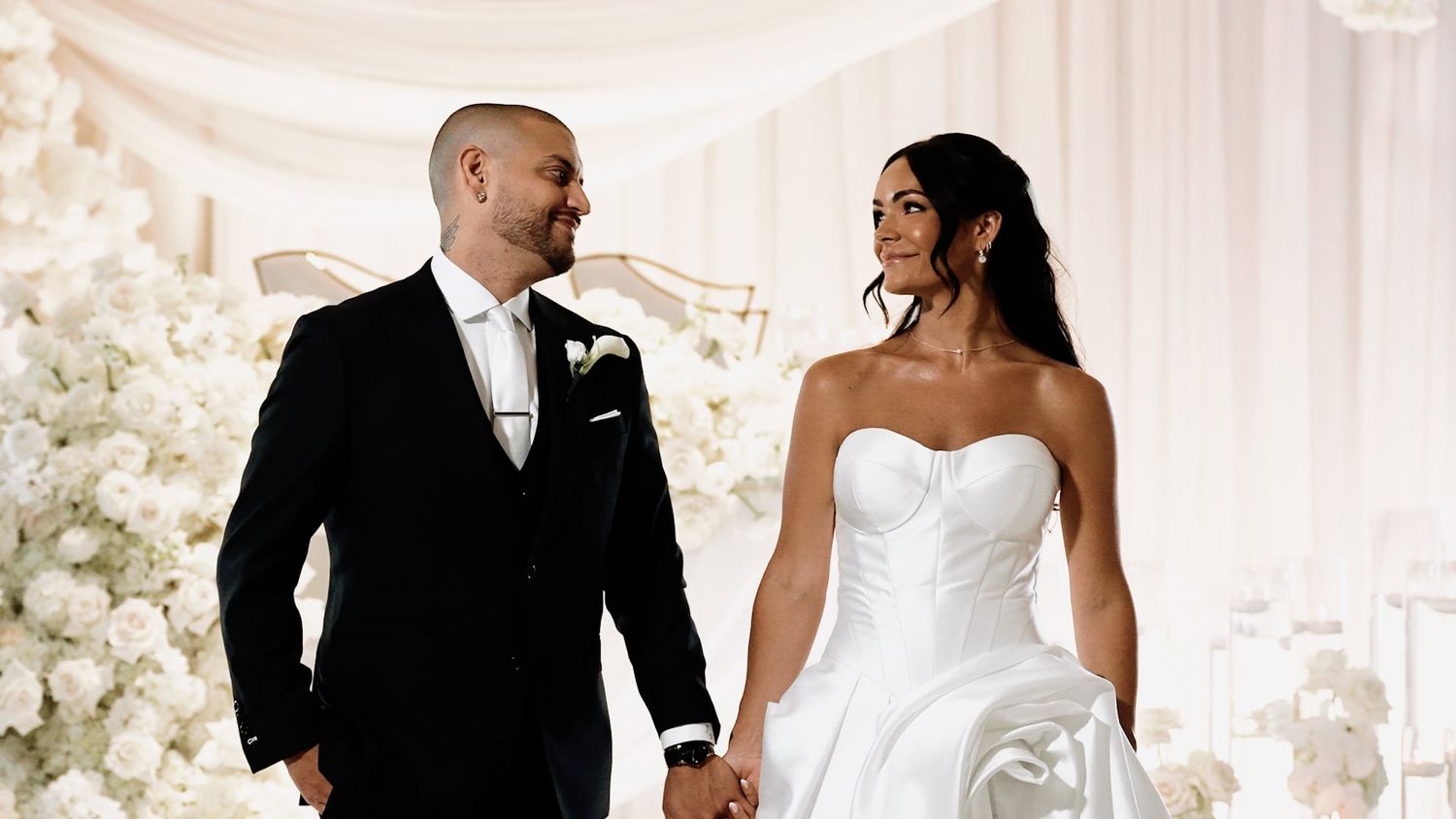 Wedding celebration in an elegant white-decorated venue with floral arrangements.