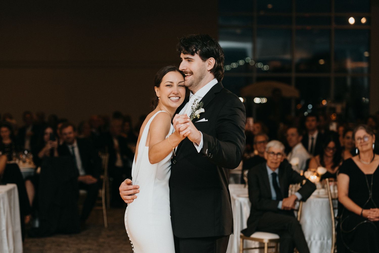 Couple dancing at wedding reception surrounded by guests in elegant venue.