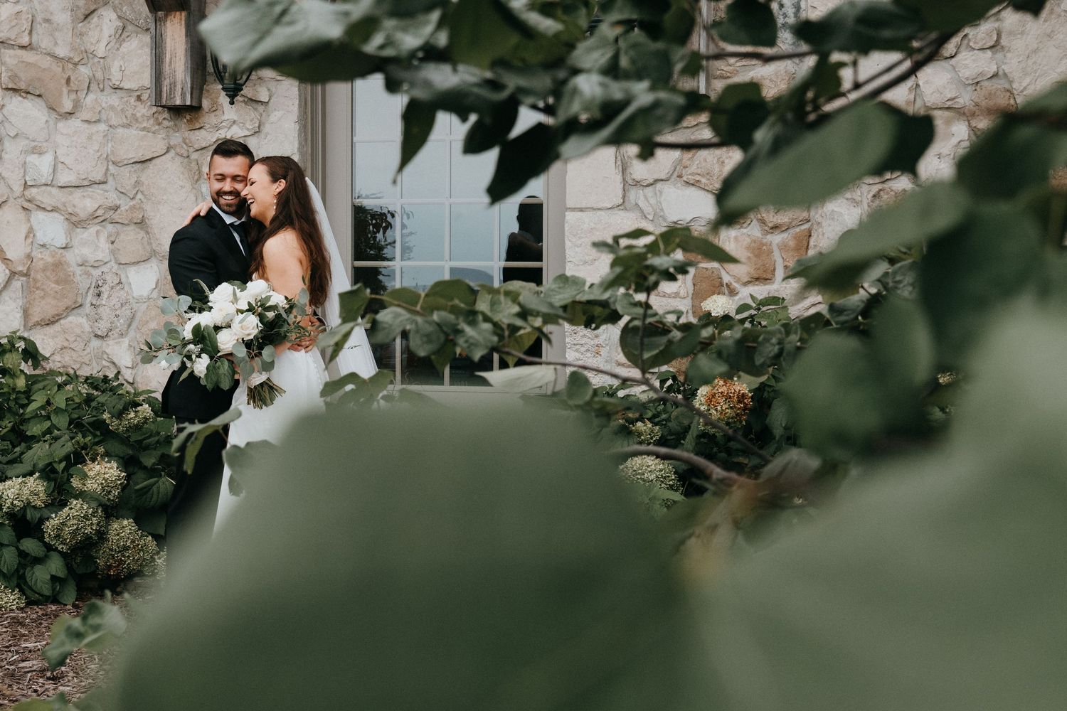Couple embracing in a romantic garden setting with stone walls and lush greenery.