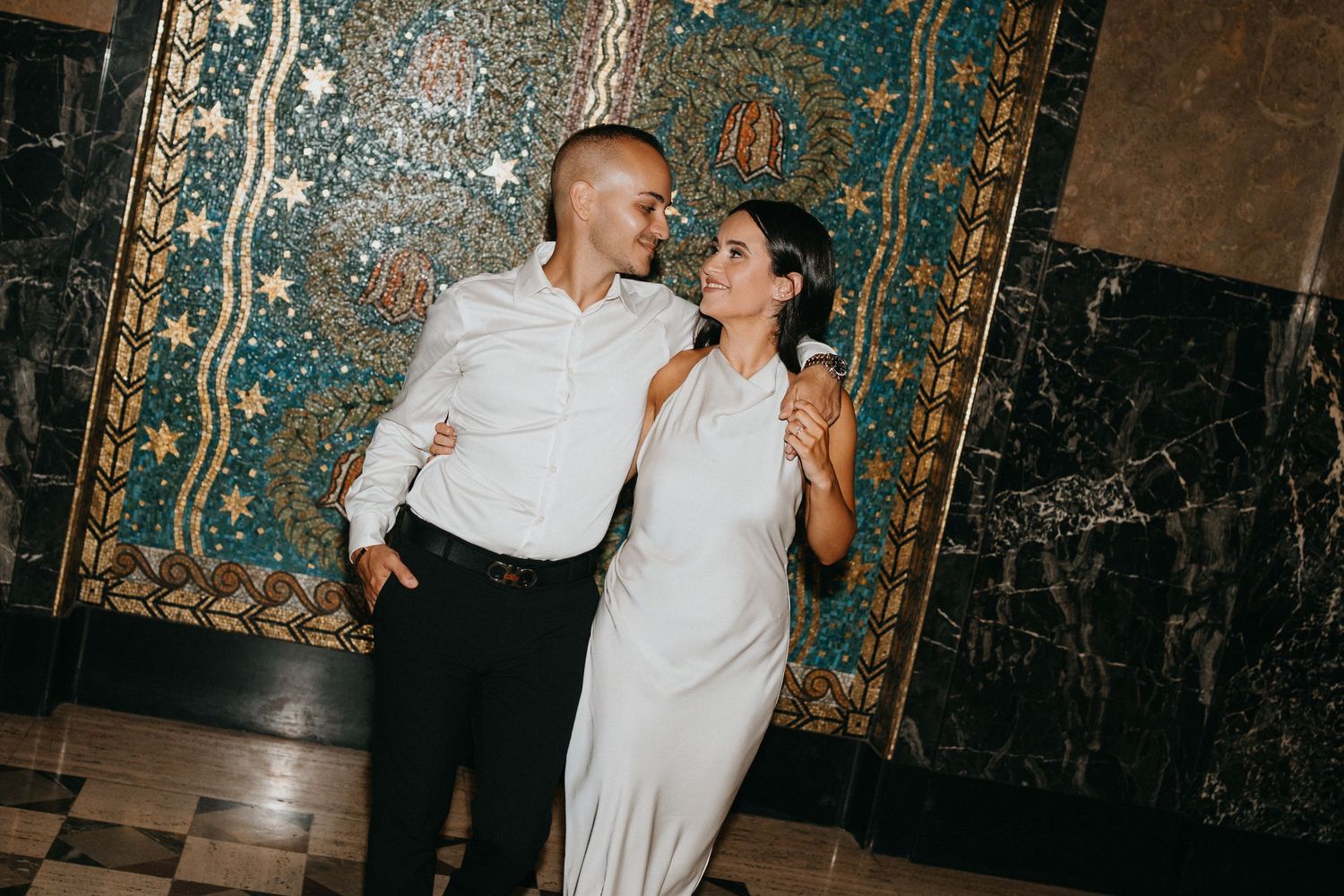 Couple dances in ornate venue with blue and gold patterned walls.