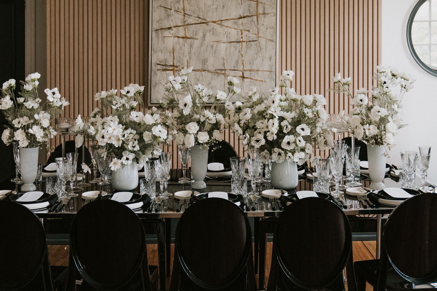 Long dining table decorated with white floral centerpieces and elegant place settings in a modern rustic venue.