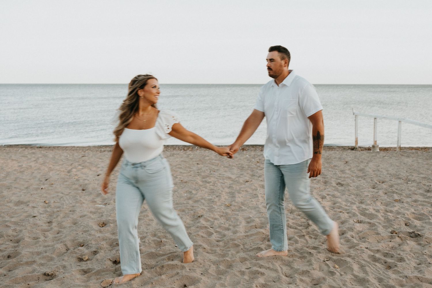 A couple dances playfully on the beach wearing coordinated white and light blue outfits.