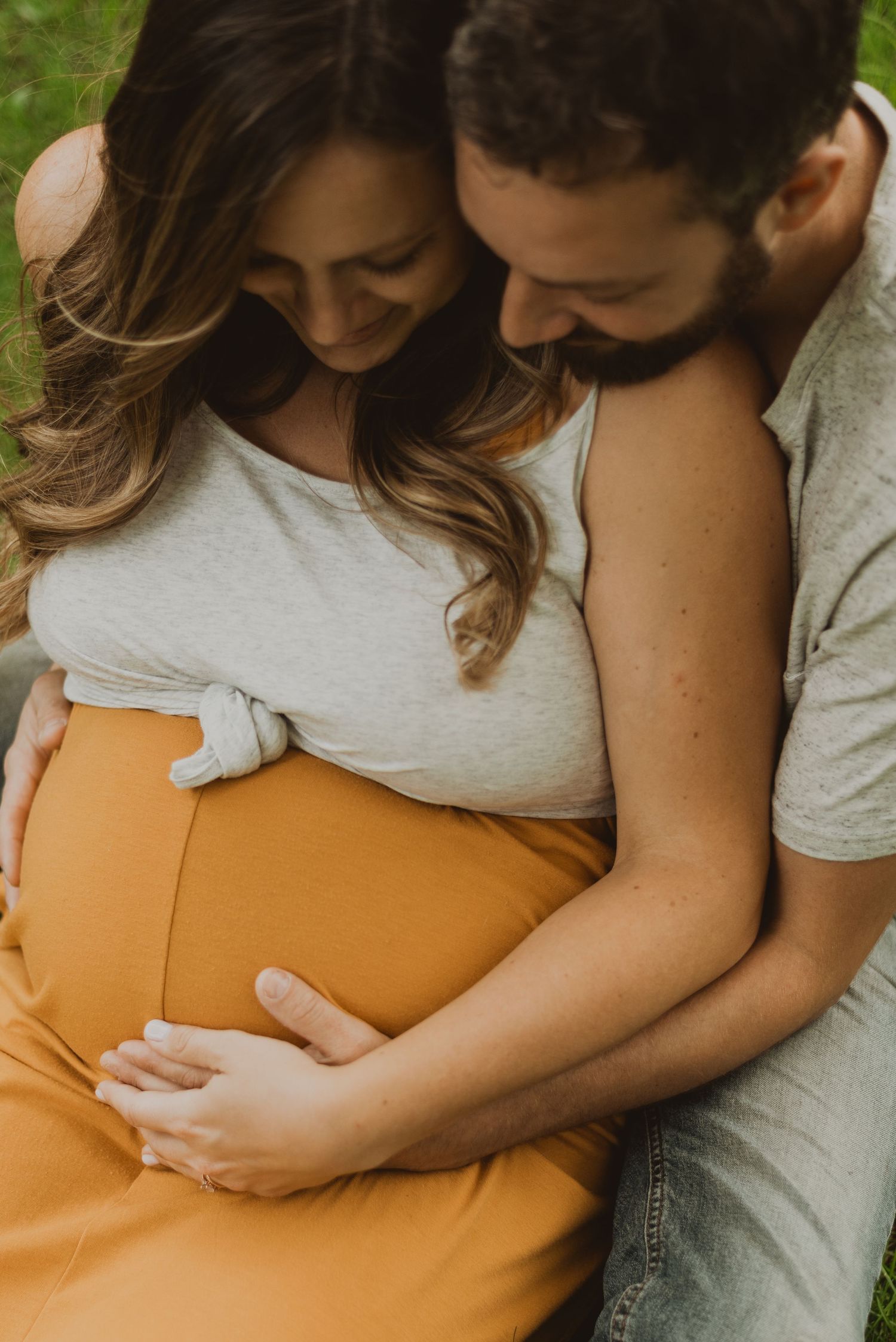 A couple tenderly cradles a pregnant belly outdoors, sharing an intimate maternity moment together.