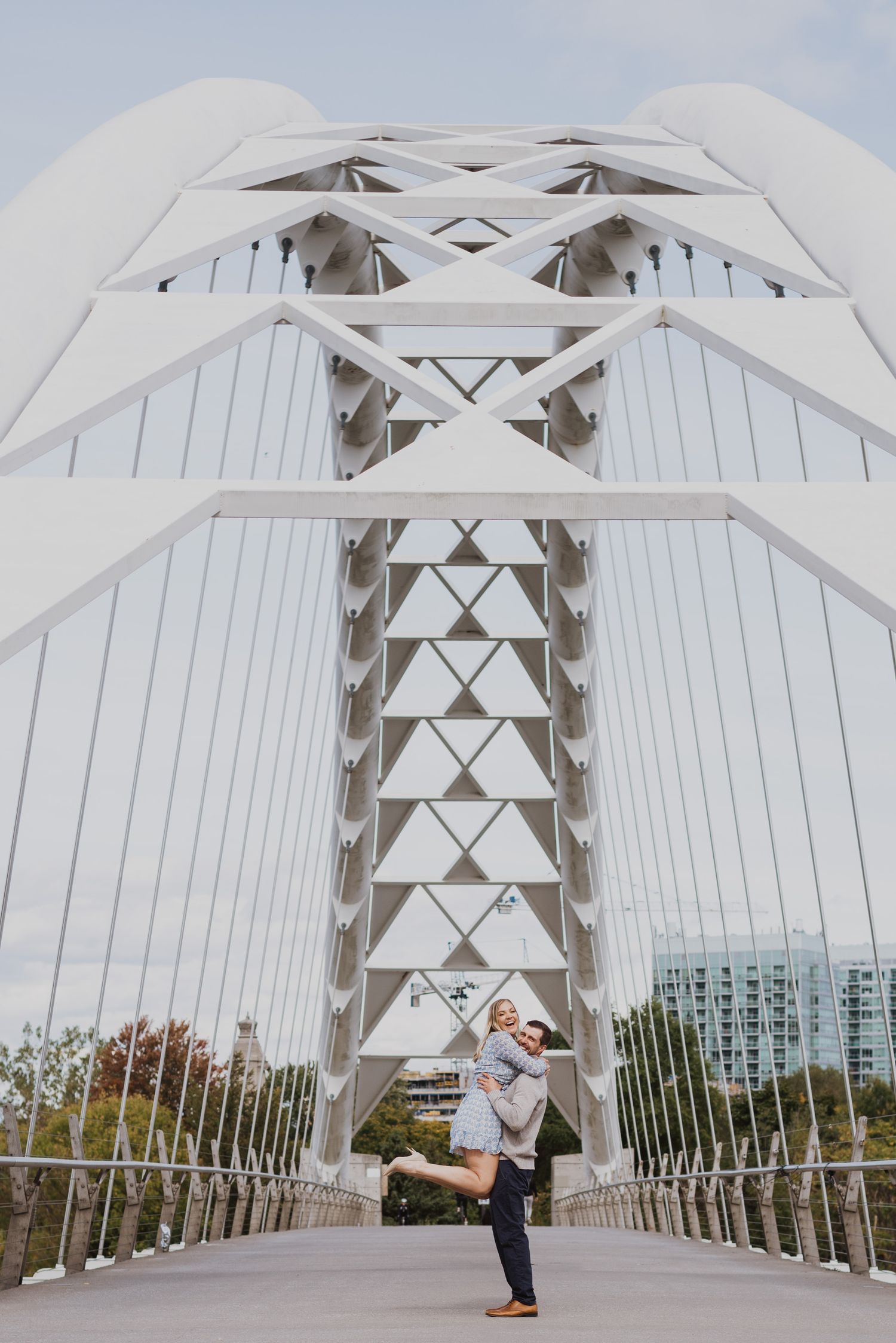 Couple embracing on a white suspension bridge with geometric steel architecture.