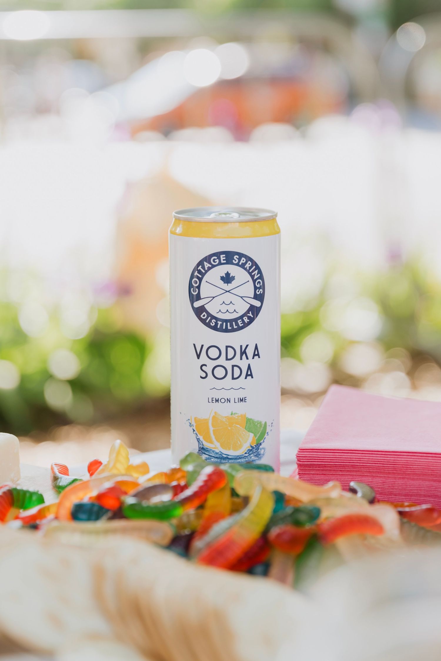 Cottage Springs Distillery Lemon Lime Vodka Soda can beside colorful gummy candies and pink napkins at an outdoor event.
