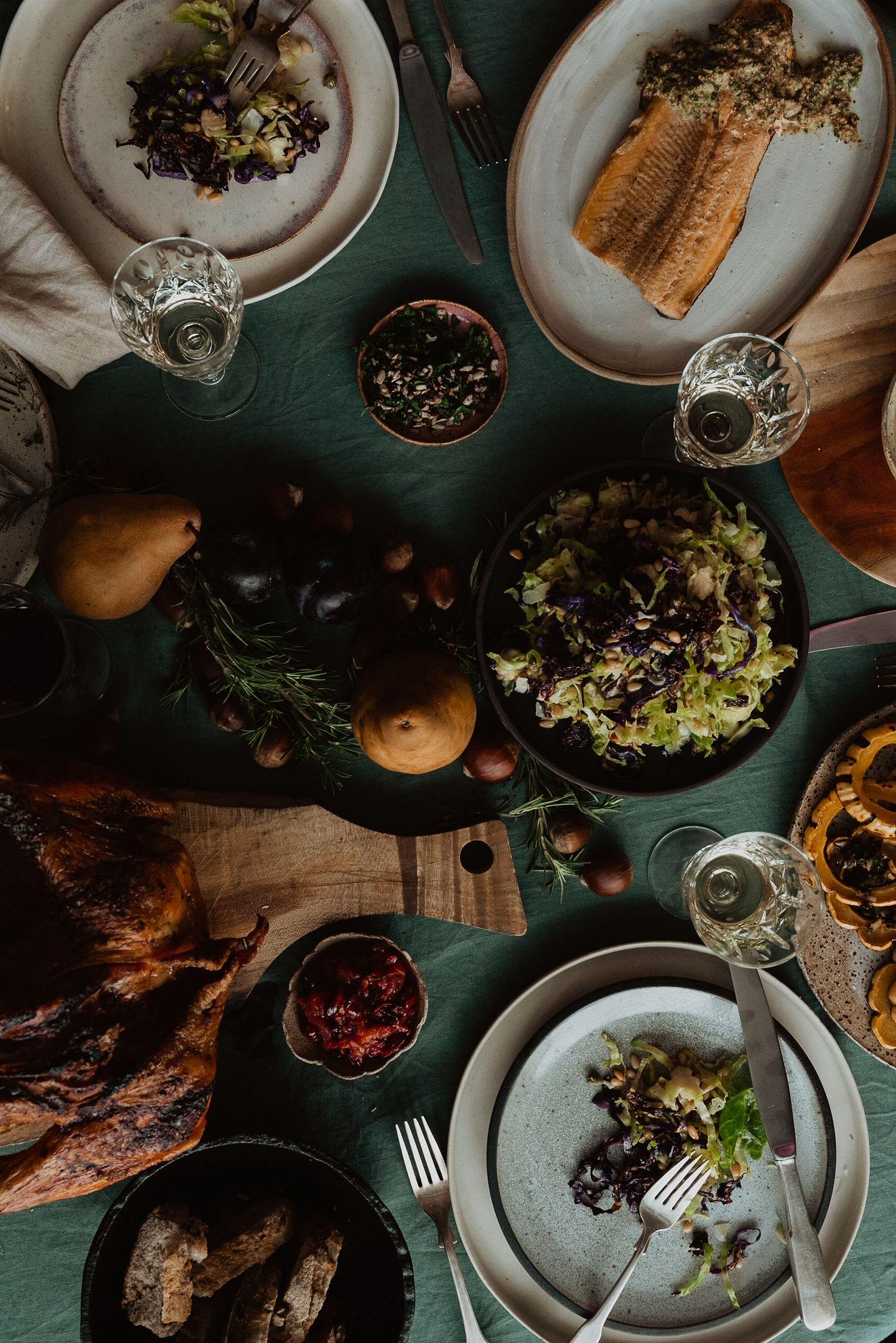 Overhead view of an elegant holiday dinner table spread with roasted turkey, salads, and seasonal dishes on a green tablecloth.