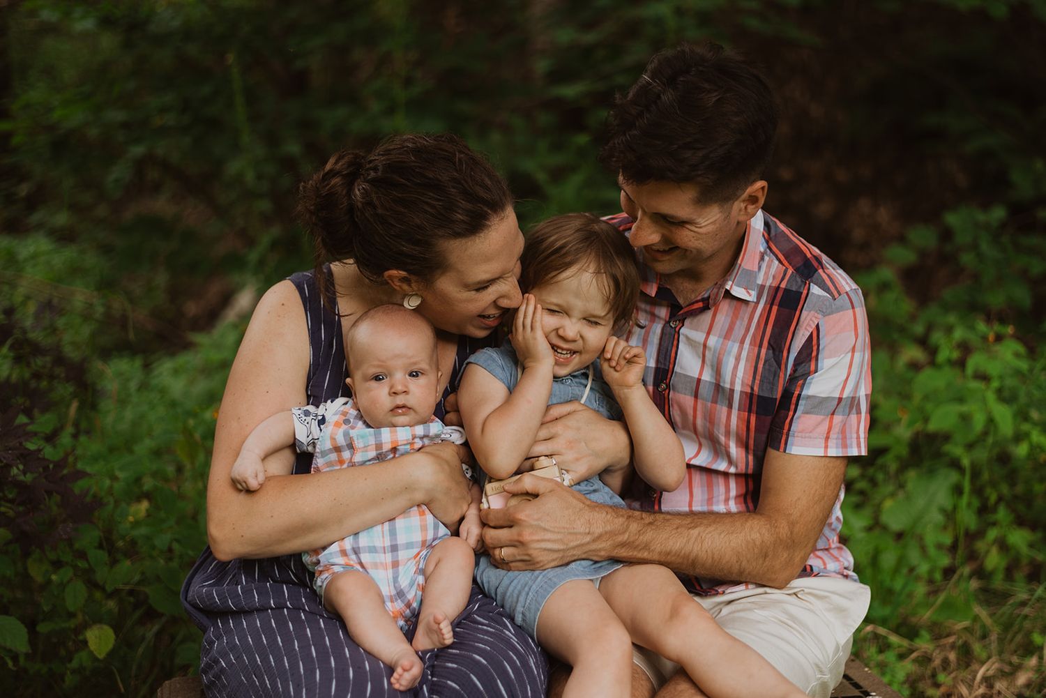 Family of four sharing intimate moment outdoors in natural setting.