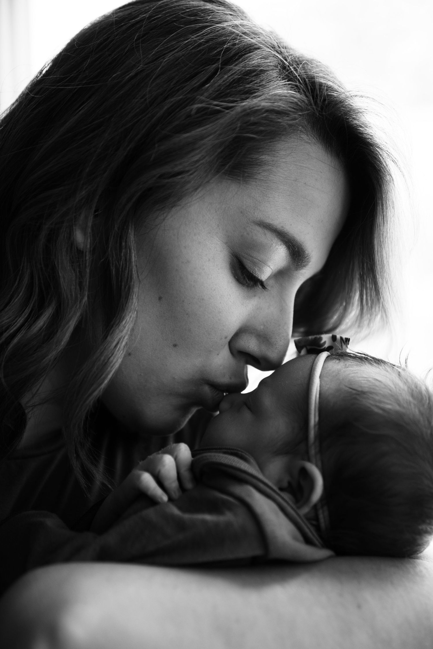 Black and white photo of a mother tenderly kissing her newborn baby, a heartfelt moment of maternal love.