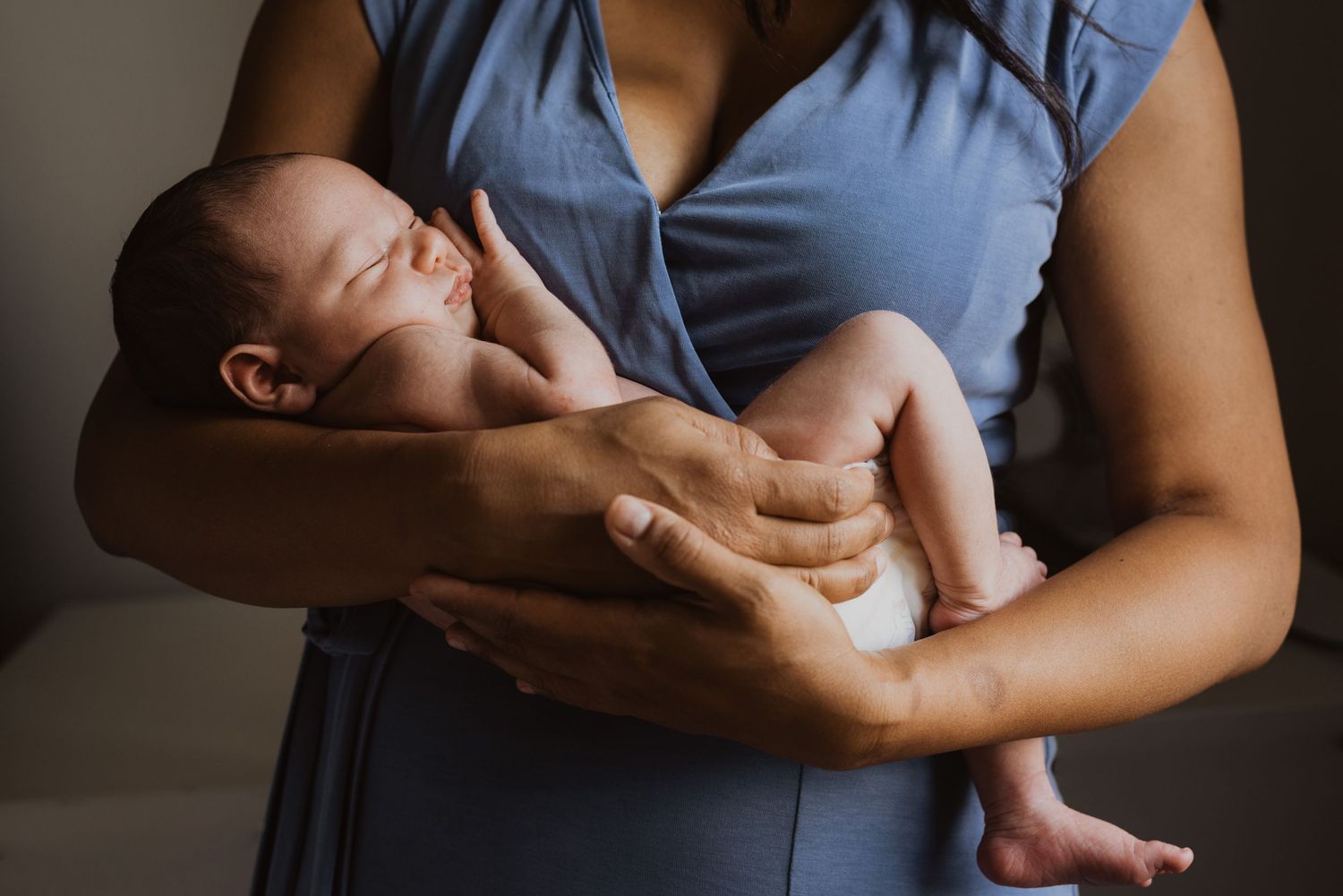 A mother in a blue dress tenderly cradles her sleeping newborn baby in her arms.