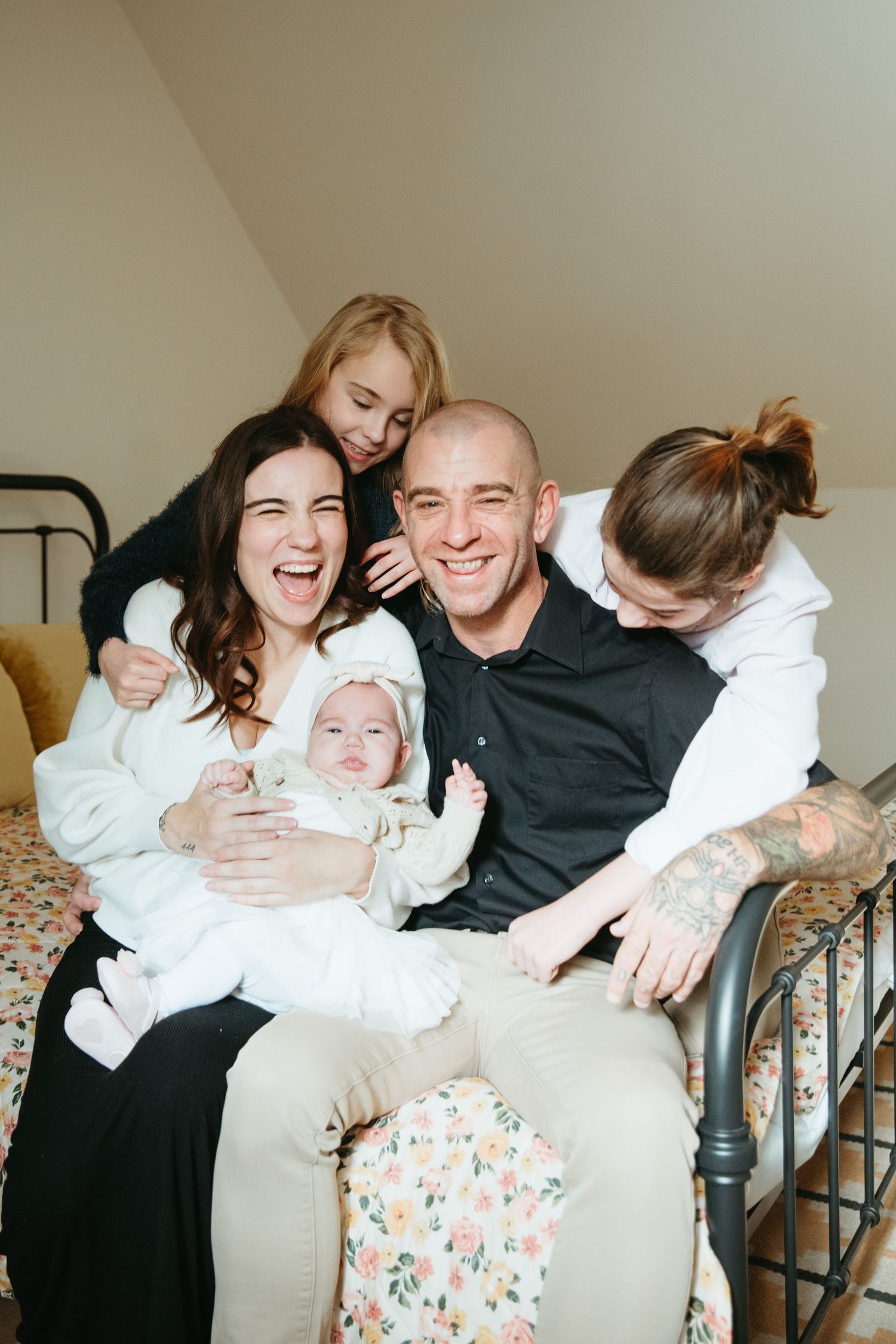 Happy family with parents, three children, and a newborn baby posing together on a bed in a cozy bedroom.