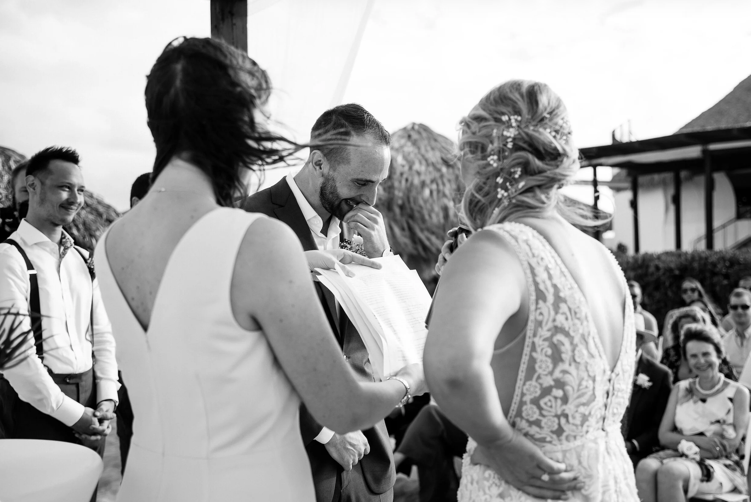 Black and white wedding ceremony photo with bride, groom, and officiant exchanging vows outdoors.