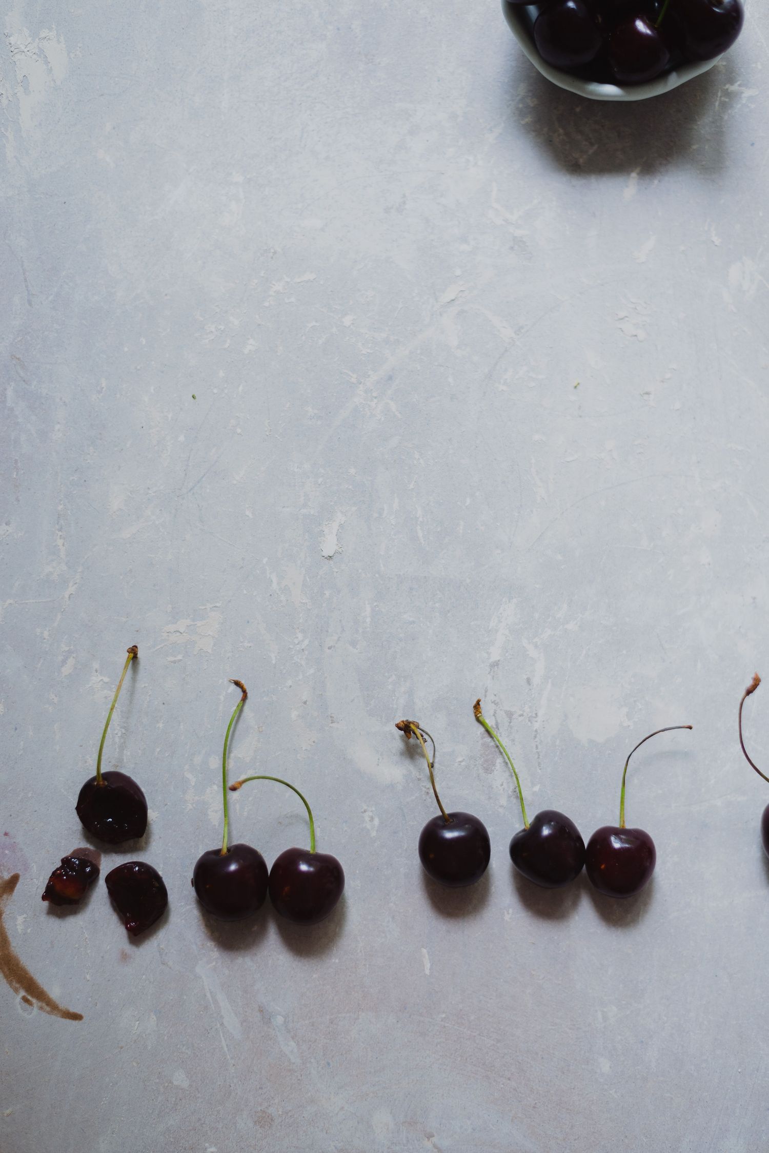 Fresh dark cherries with stems arranged in a row on light gray marble surface.