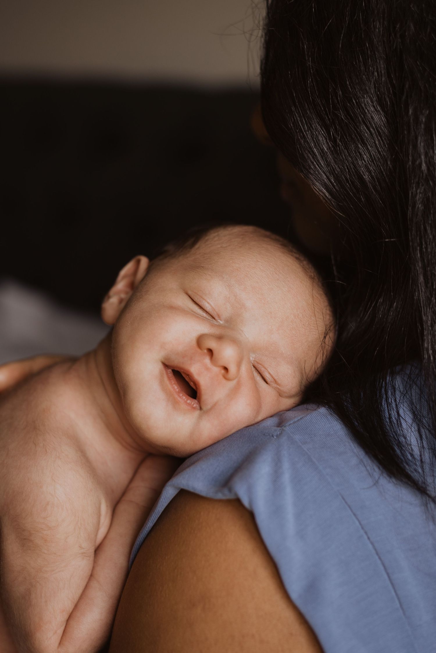 A newborn baby resting on mother's shoulder, eyes closed, with a peaceful expression in soft natural light.