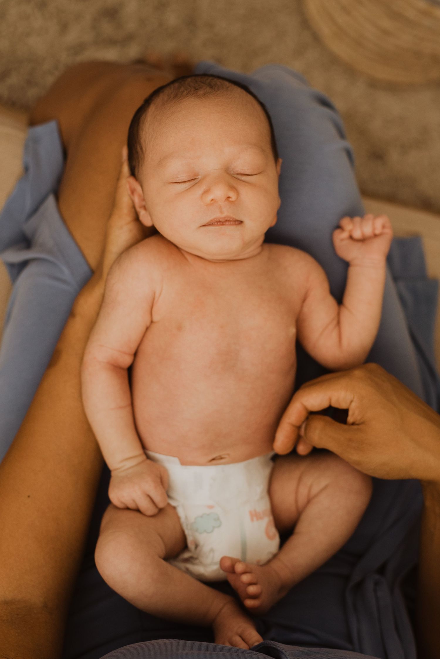 Newborn baby in diaper resting peacefully in parent's arms on a soft blue blanket.