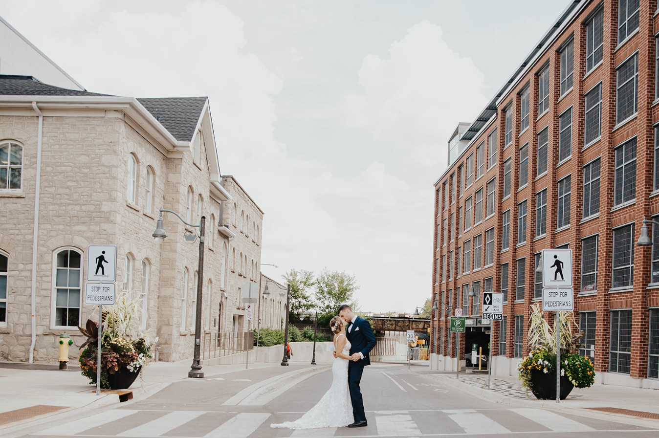 Bride and groom share a romantic kiss on a charming brick street between historic buildings on their wedding day.