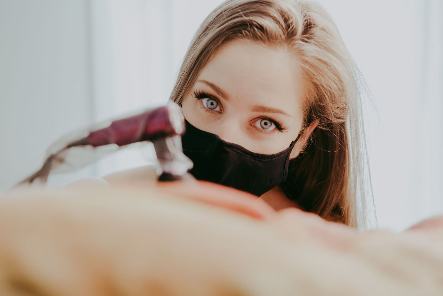 Close-up of a blonde woman wearing a black face mask holding a tattoo gun, preparing to work.