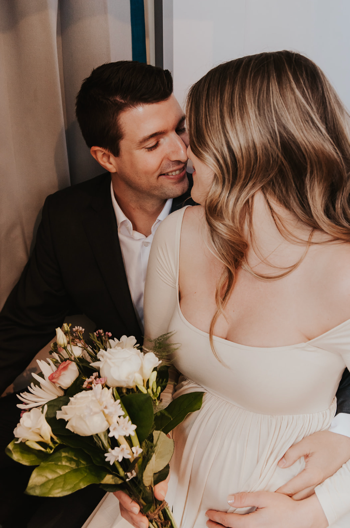 A couple in wedding attire shares a romantic moment, the bride holding a bouquet of white flowers.