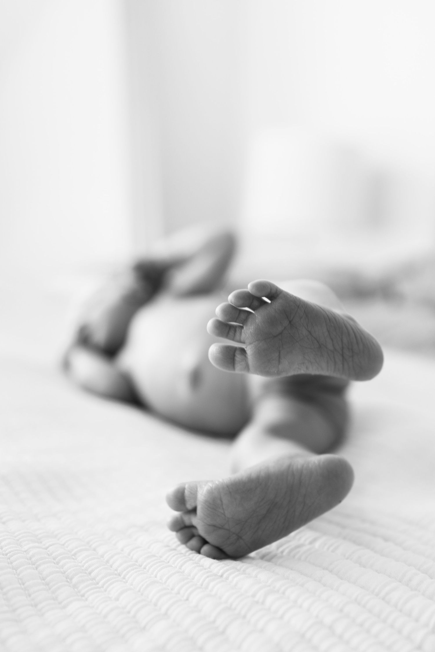 Black and white close-up of newborn baby feet lying on a soft white blanket.