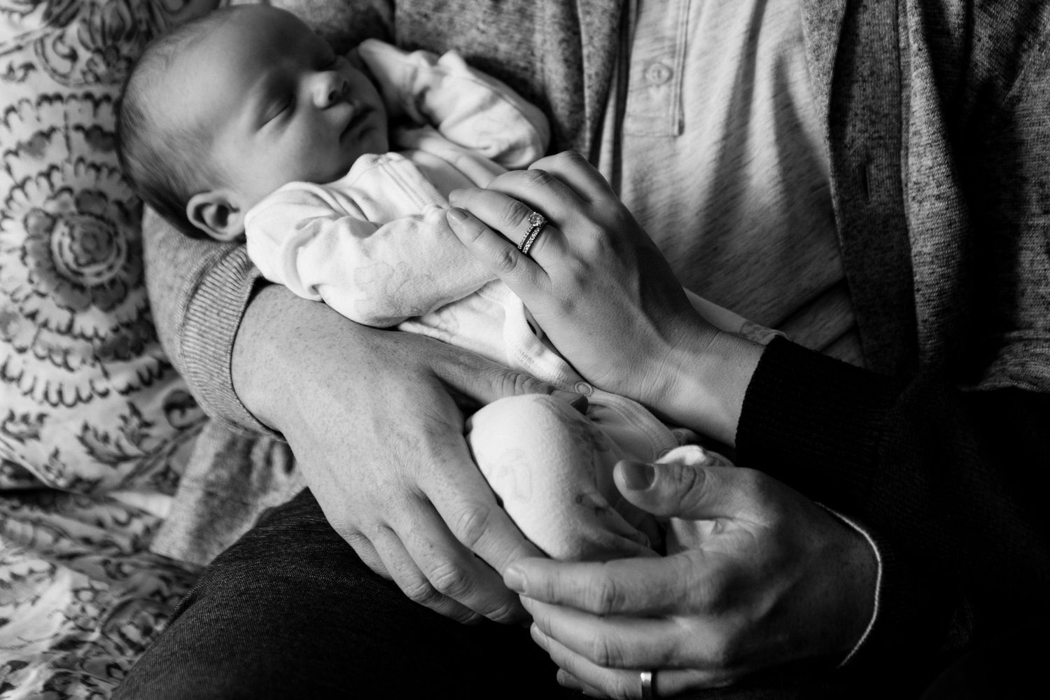 Black and white photo of a newborn baby cradled in adult hands, peaceful and serene family moment.