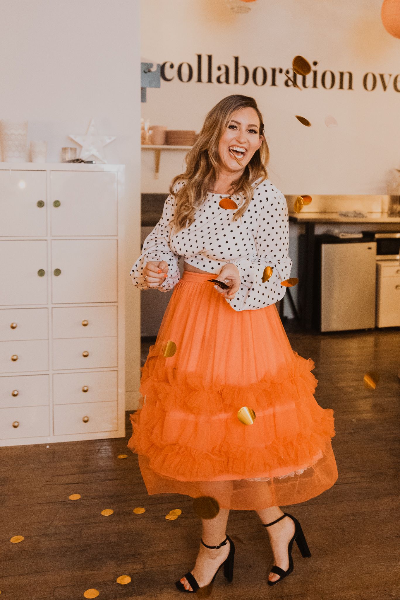 Woman in orange tulle skirt and polka dot blouse laughing at a collaboration party event with confetti.