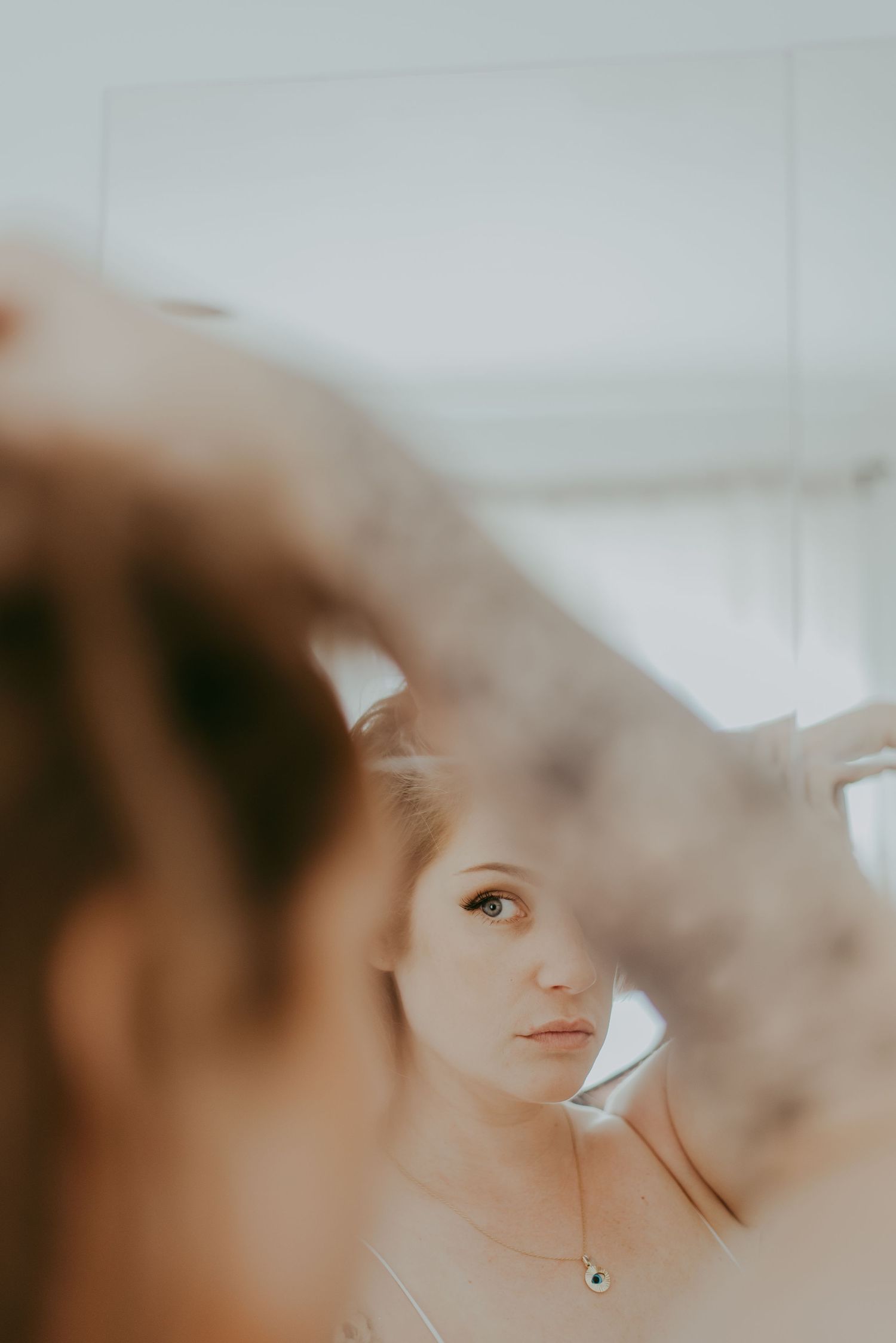 Young woman with a necklace gazes into a mirror, her reflection captured in a soft, dreamy light.