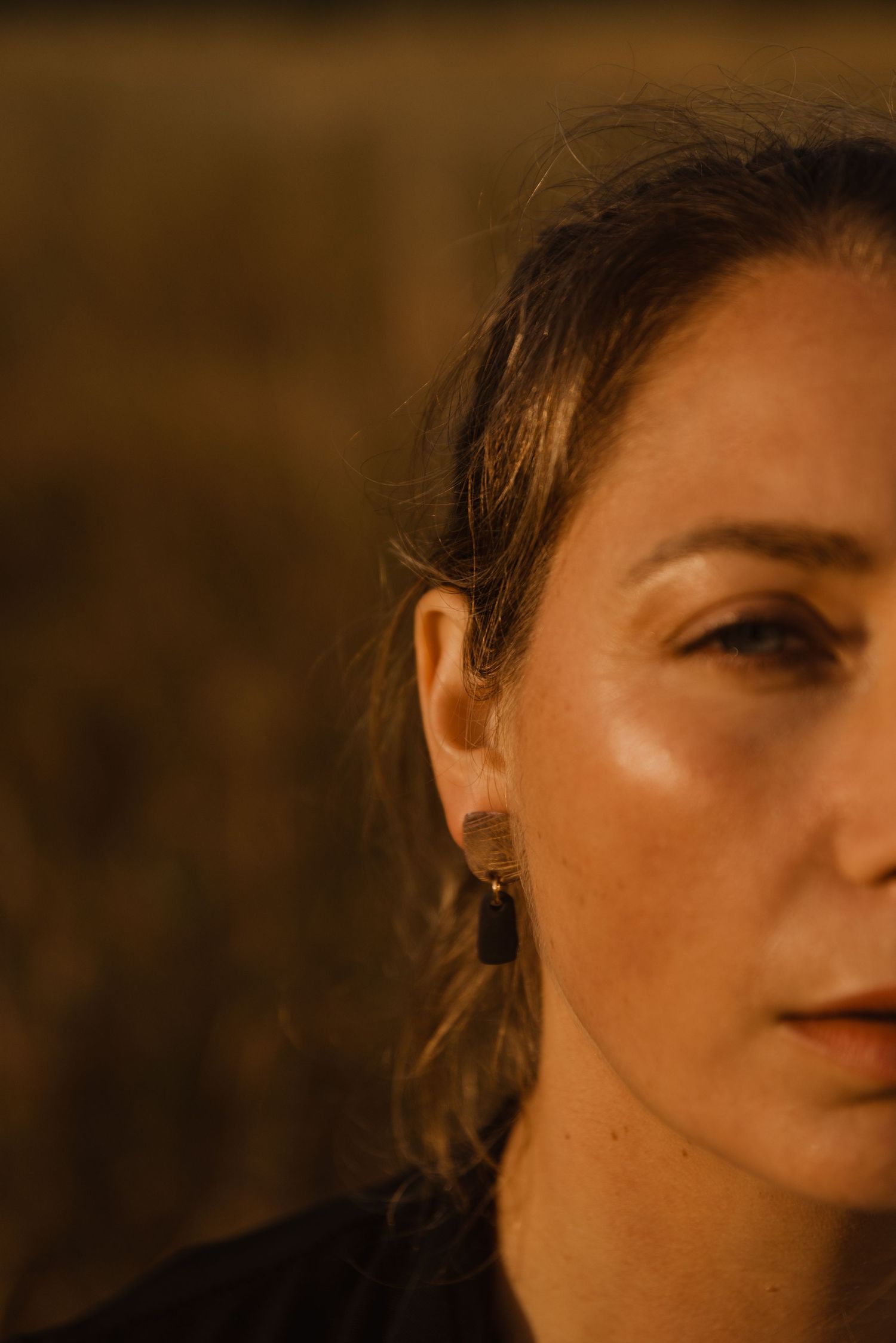 Close-up portrait of a middle-aged woman with dark hair, wearing drop earrings, photographed in warm golden light.