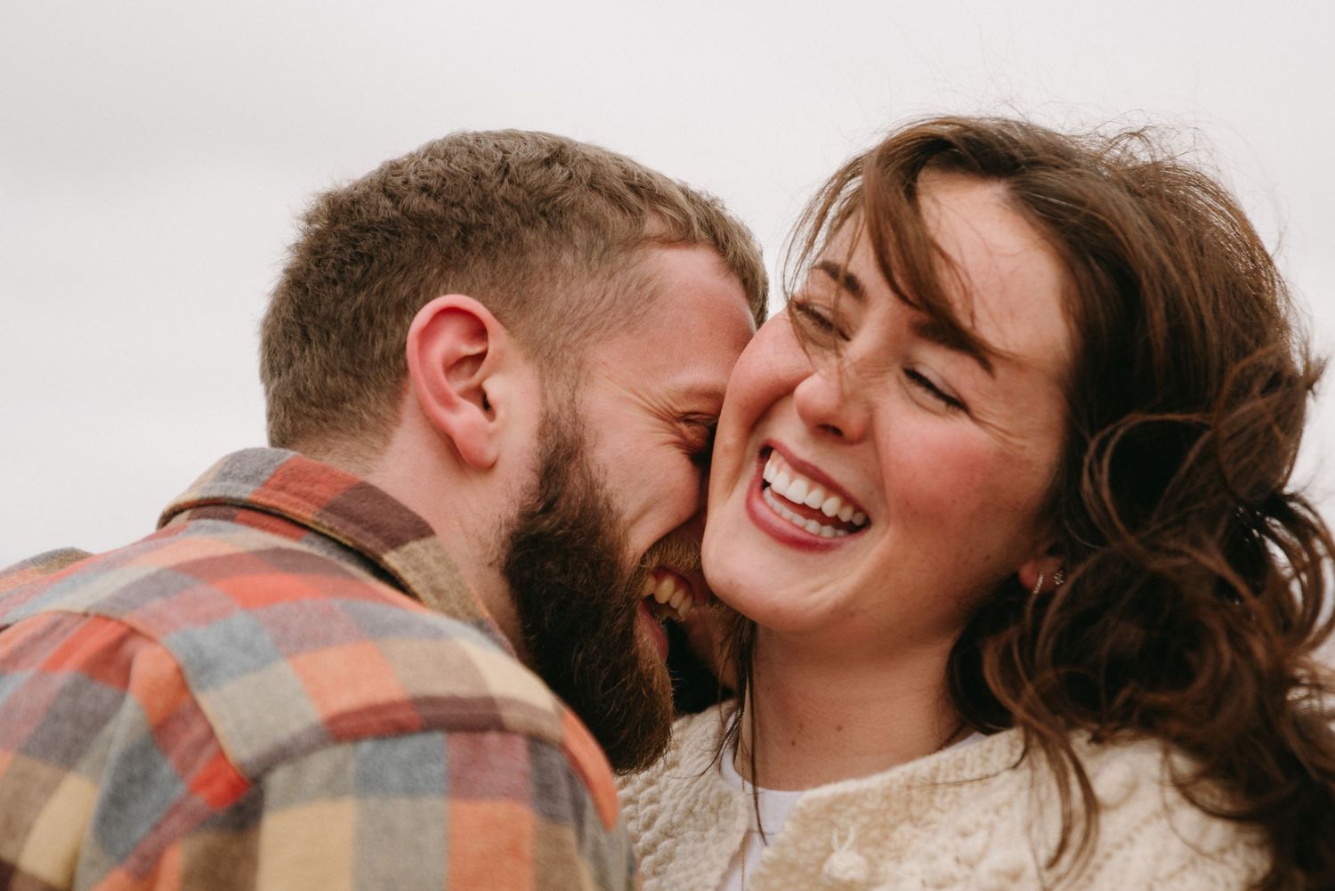 Happy couple sharing a tender moment, man whispering in laughing woman's ear outdoors.