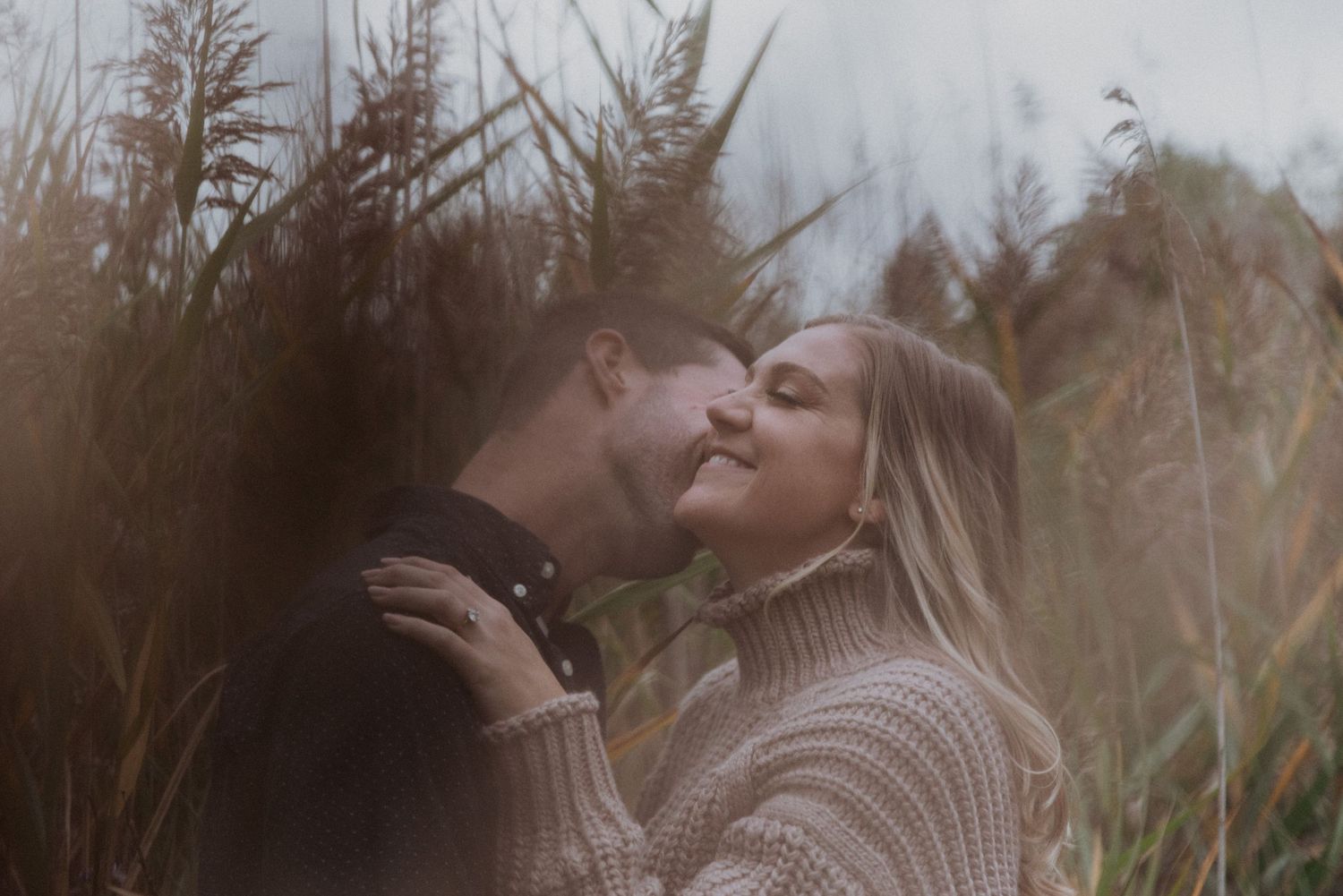 Romantic couple sharing a tender kiss surrounded by tall golden grasses in nature.
