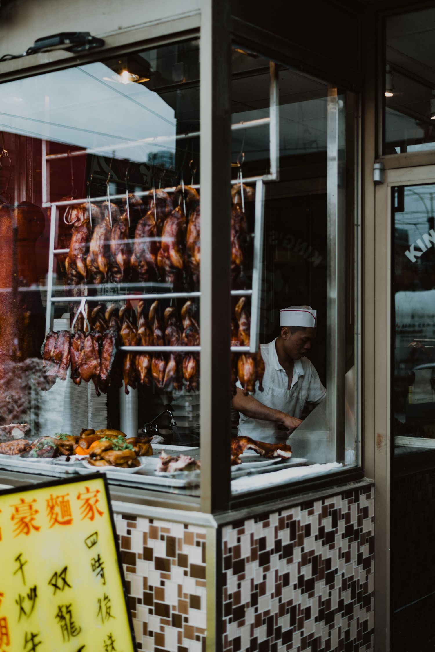 Chinese BBQ shop window displaying hanging roasted ducks and meats with a chef working inside.