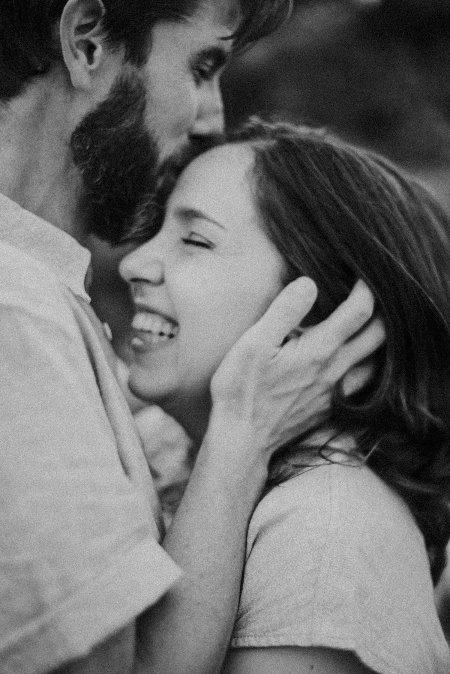 Black and white photo of a smiling woman being tenderly embraced by a bearded man holding her face.