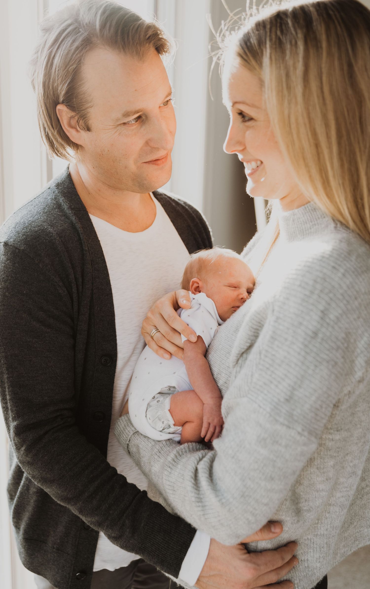 Happy parents smiling at each other while holding their newborn baby together.