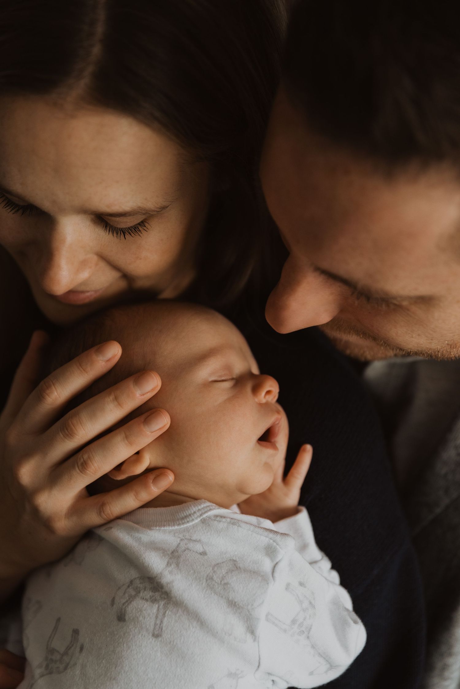 Loving parents gently kissing their sleeping newborn baby together.