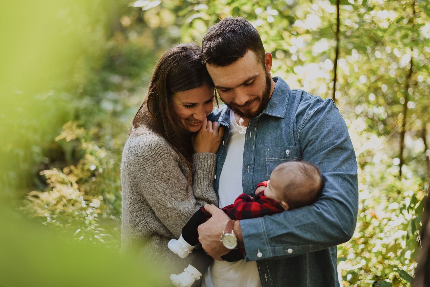 Happy couple sharing a tender moment with their newborn baby outdoors in a lush green park setting.