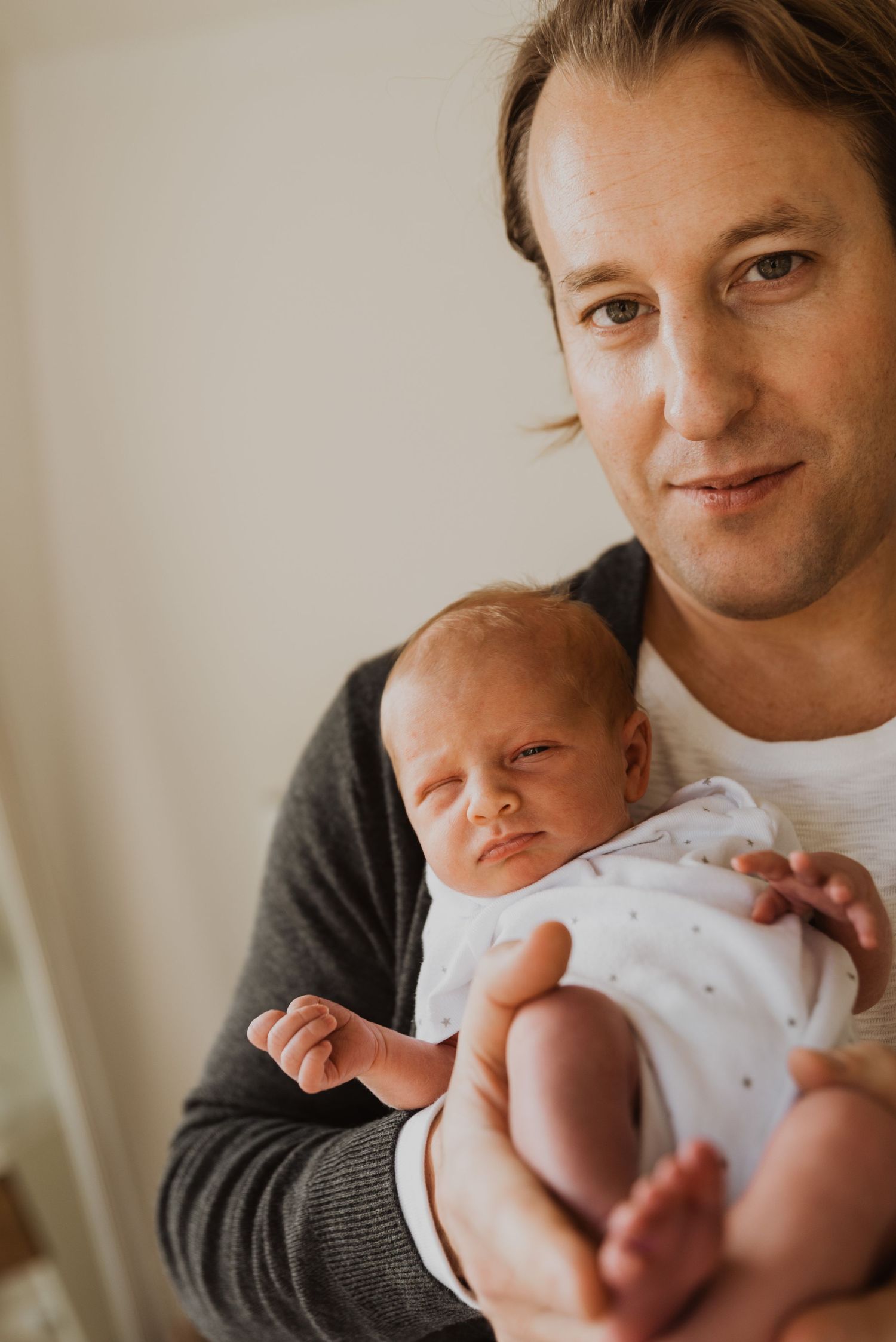 Father cradling sleeping newborn baby in arms, tender family portrait.