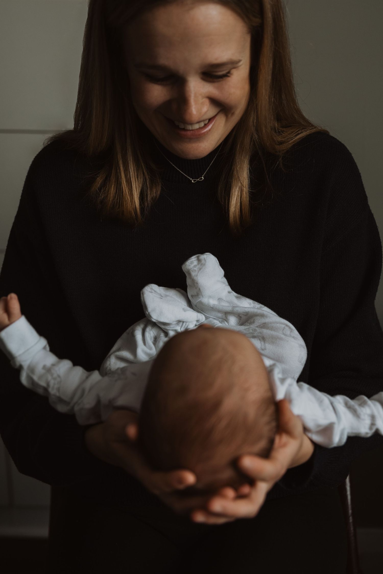 Smiling mother in black sweatshirt cradling her newborn baby in her arms.