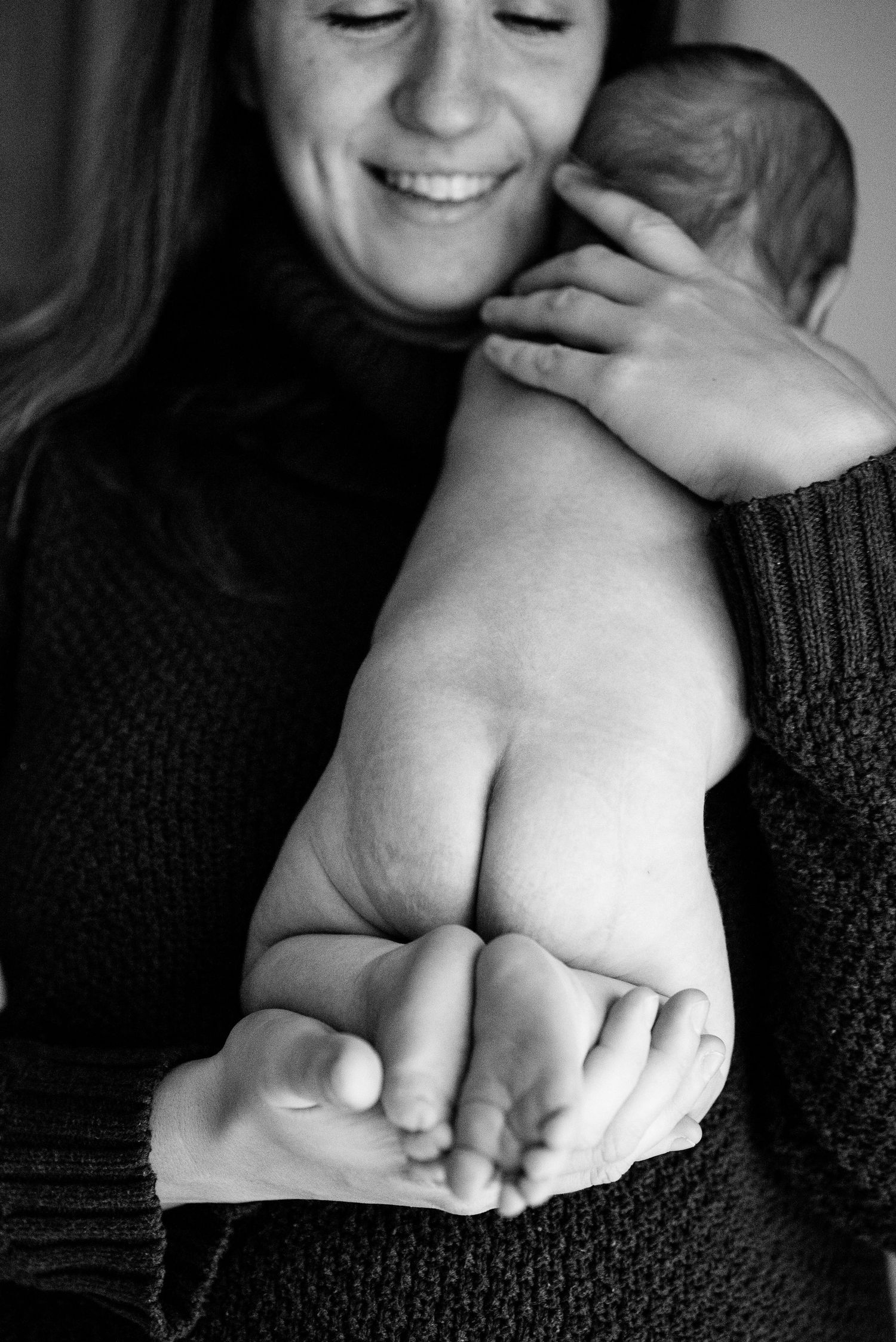Black and white photo of a smiling mother cradling her newborn baby, showing tiny feet in her hands.