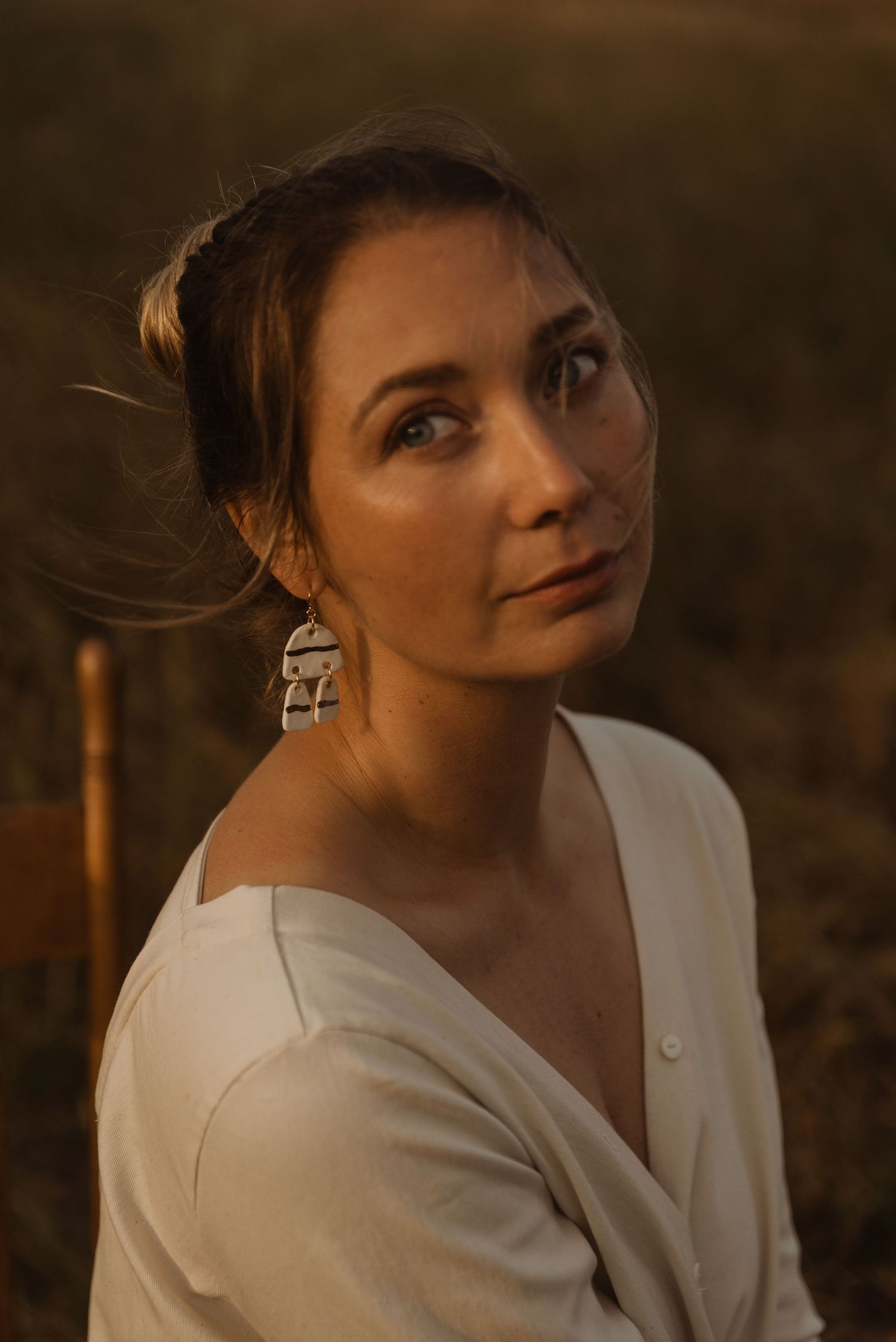 Woman in white top with silver earrings gazes upward in warm golden hour light outdoors.