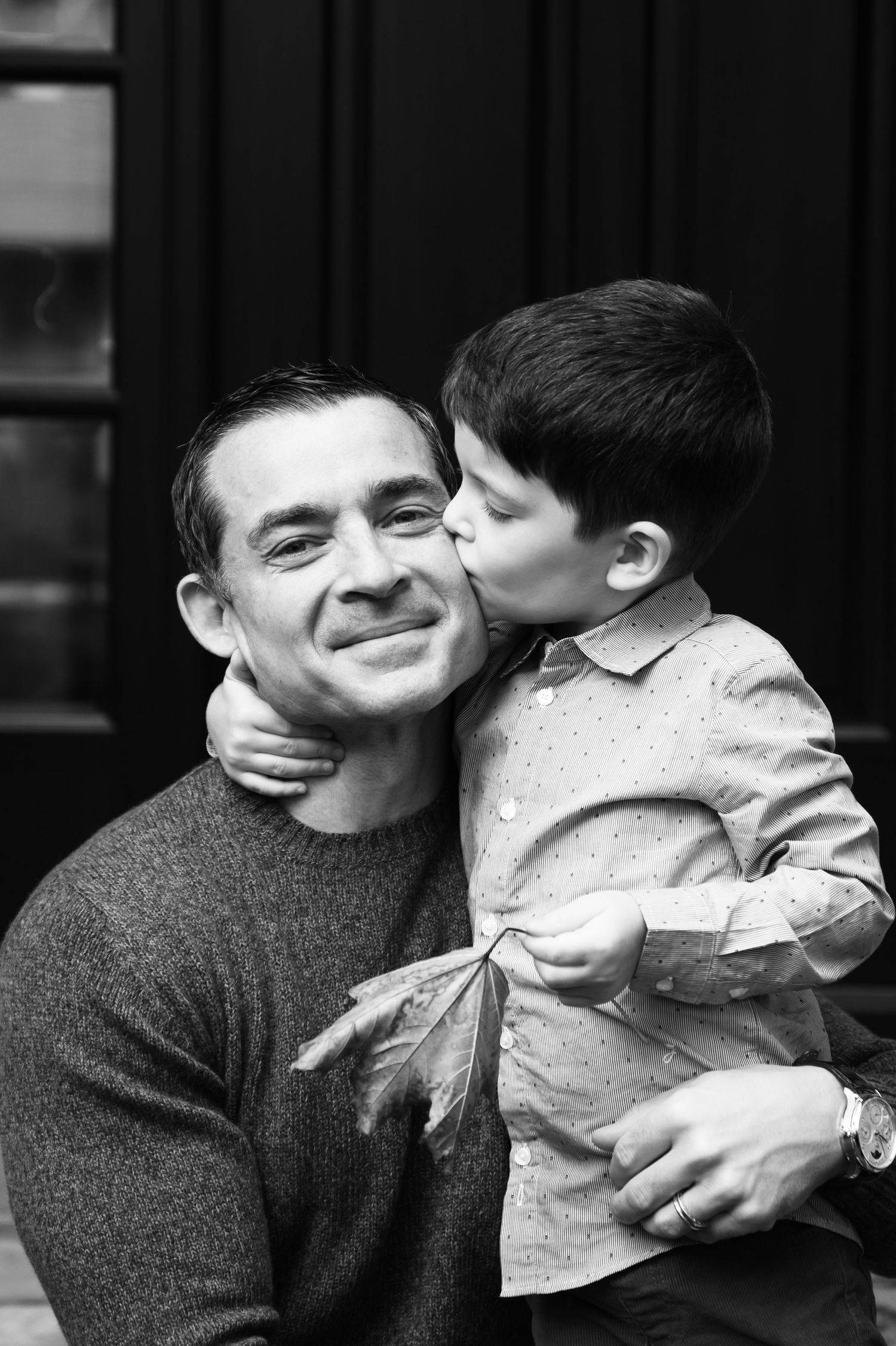 Black and white photo of a young boy kissing his smiling father on the cheek while being held.