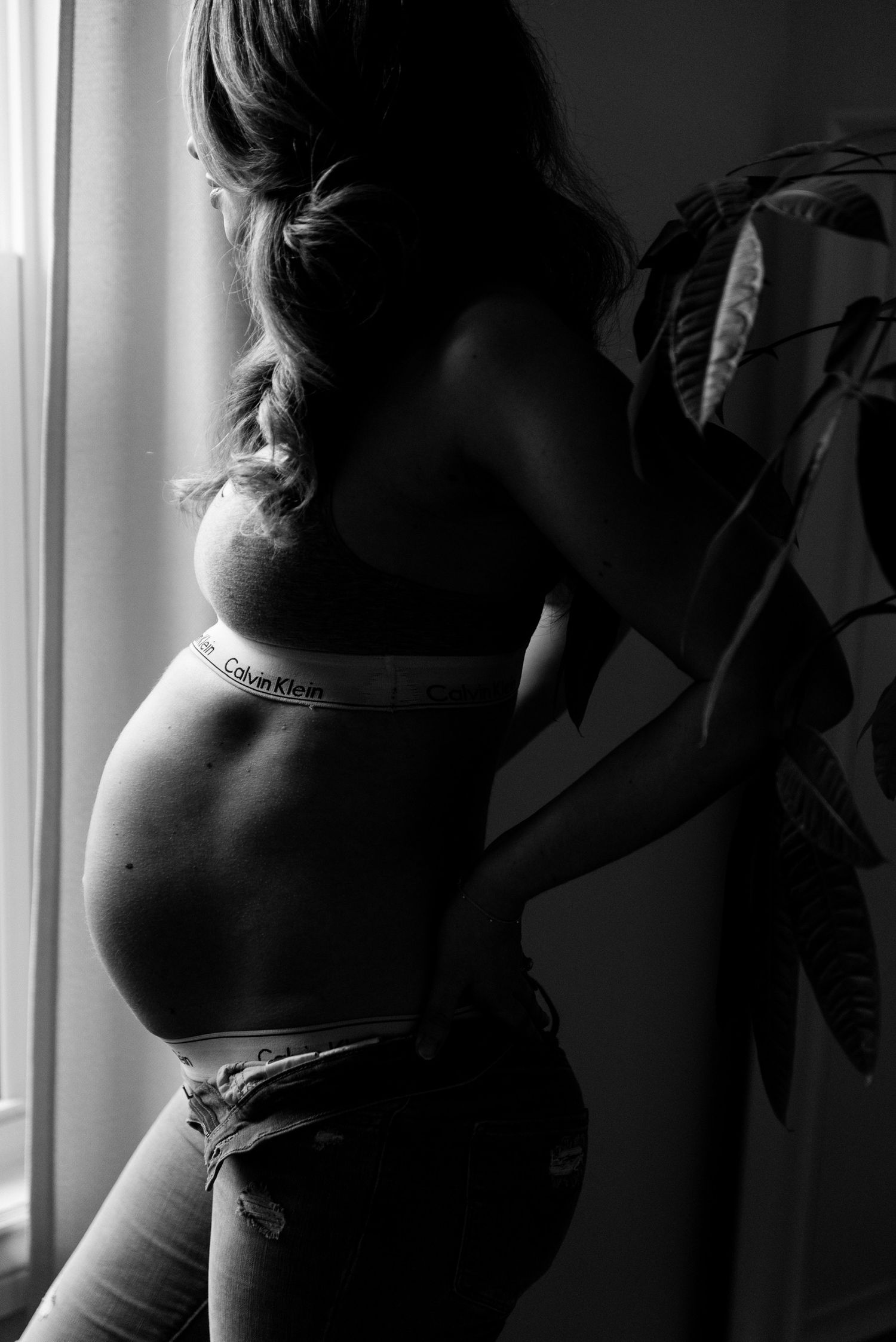 Black and white silhouette of pregnant woman in Calvin Klein underwear by window with plant.