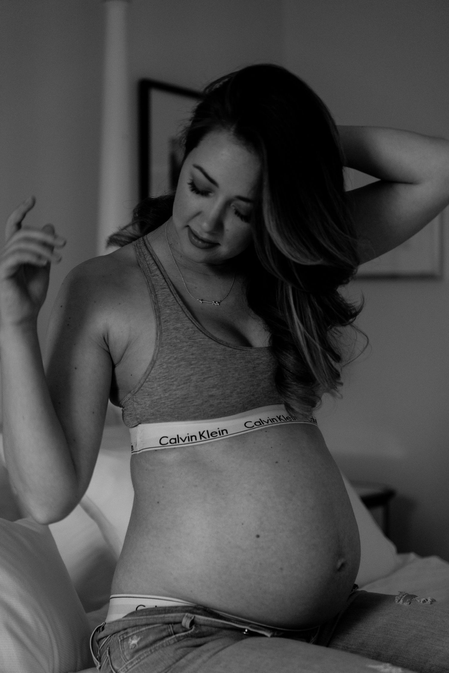 Black and white photo of a pregnant woman in Calvin Klein underwear and sports bra, looking down at her baby bump.